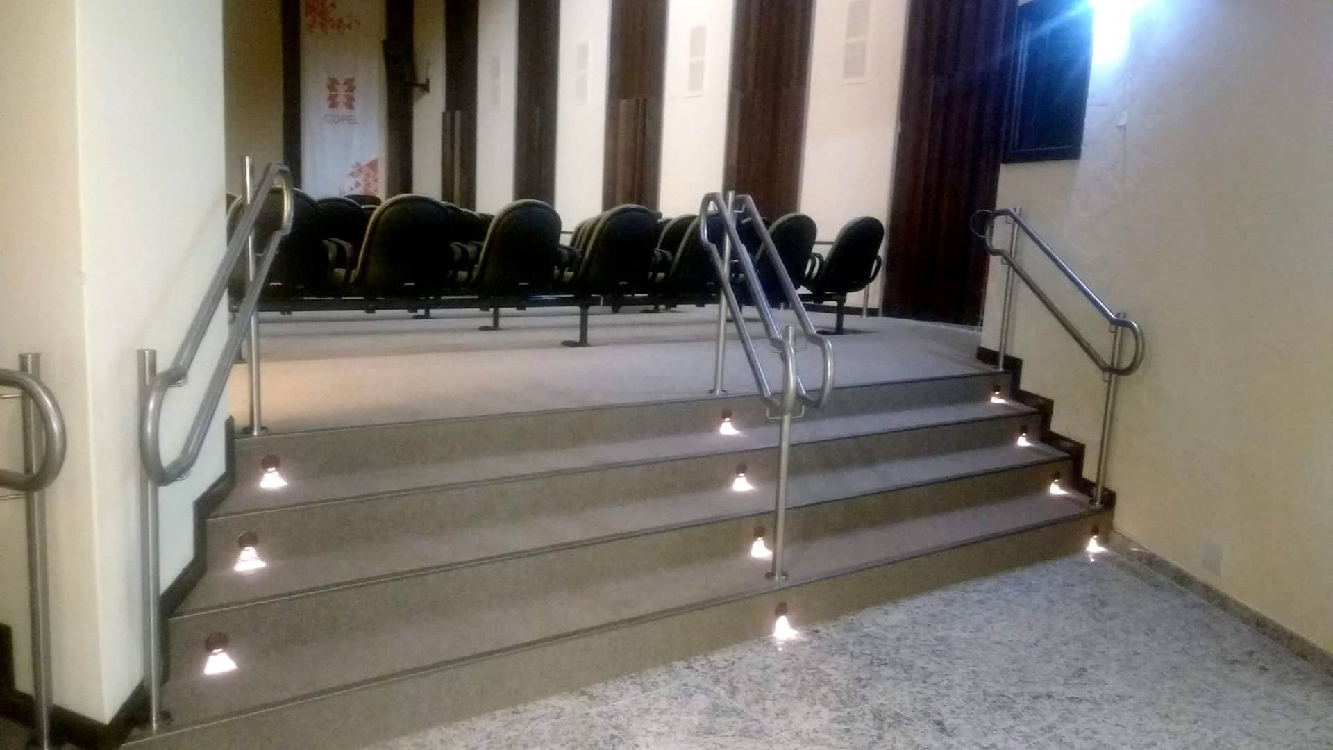 Degraus de auditório com corrimãos em inox e iluminação de piso