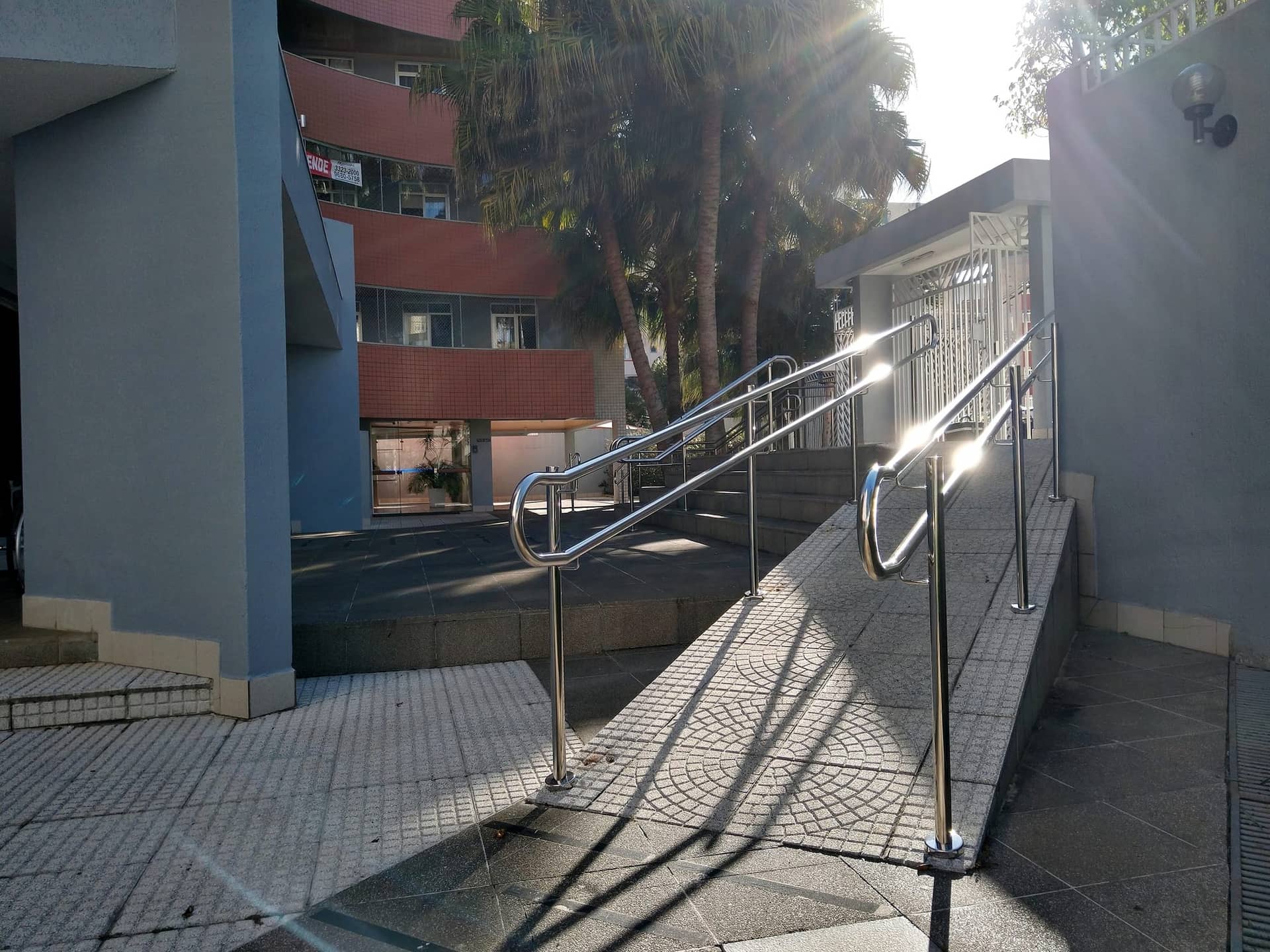 Rampa com corrimão duplo em inox entre a escada e o jardim do condomínio