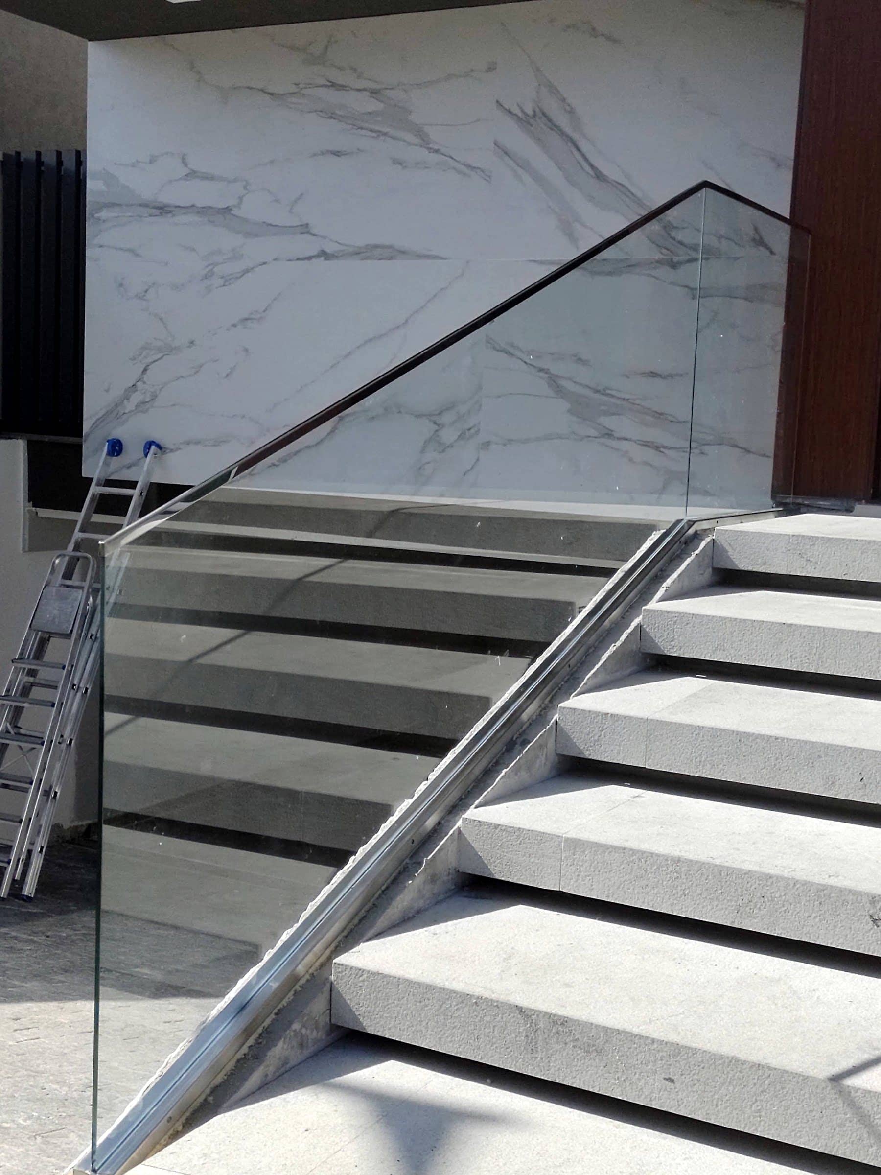 Escadaria externa com guarda-corpo de vidro e corrimão em inox ao lado de parede de mármore