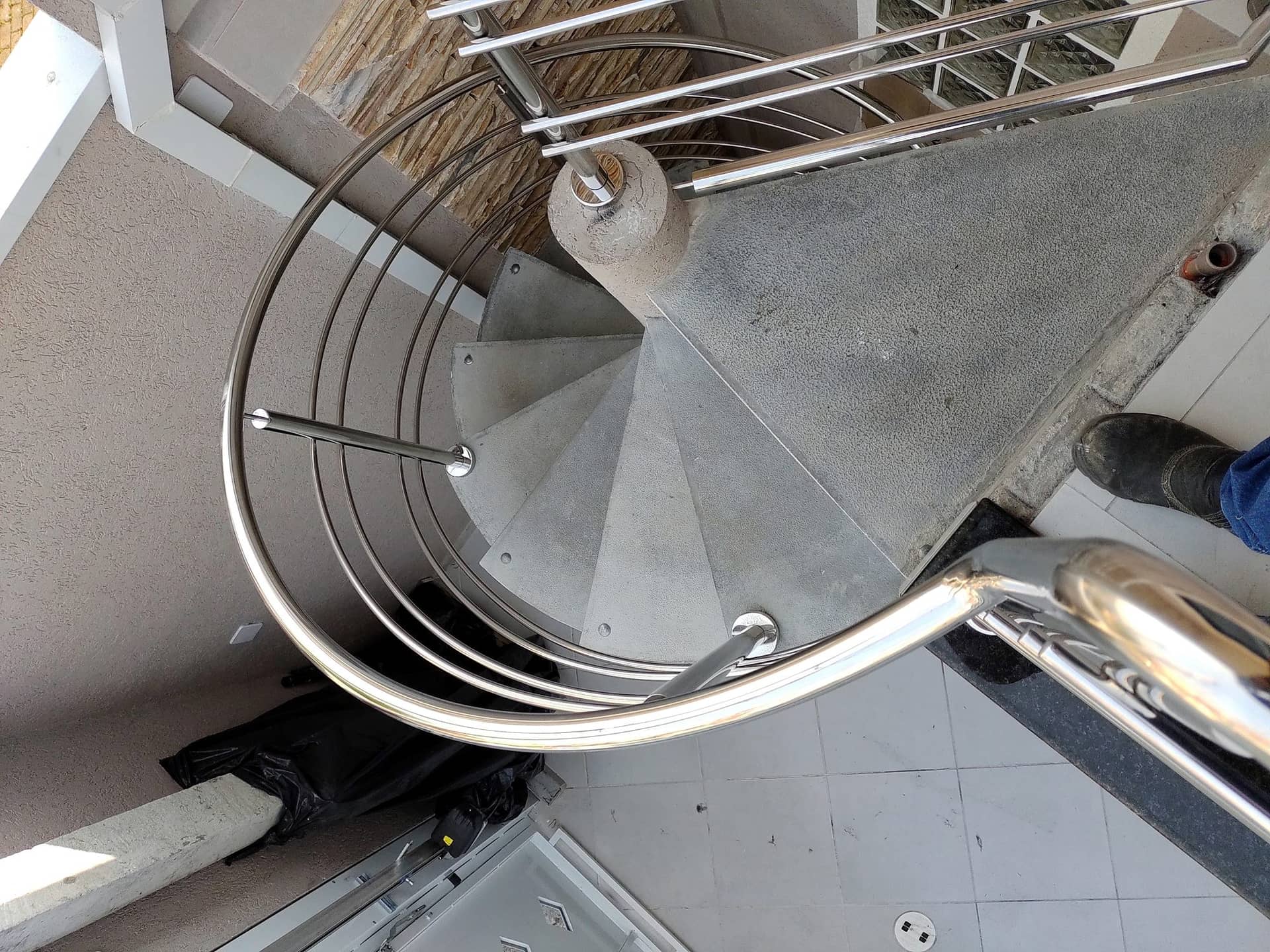 Escada caracol vista de cima, com o corrimão curvo em inox contornando o pilar central