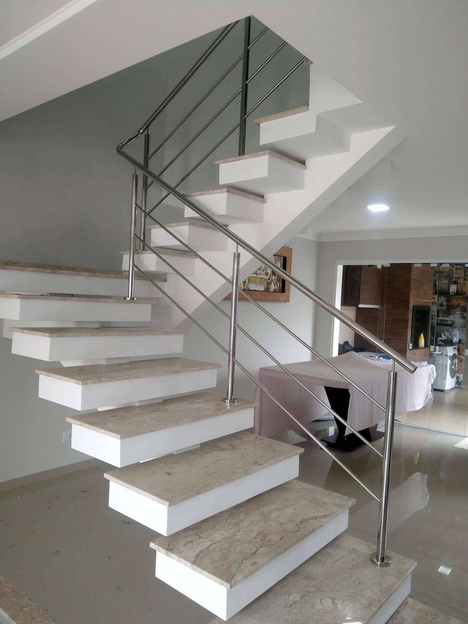 Escada em L com degraus de mármore em balanço e guarda-corpo de hastes horizontais em inox