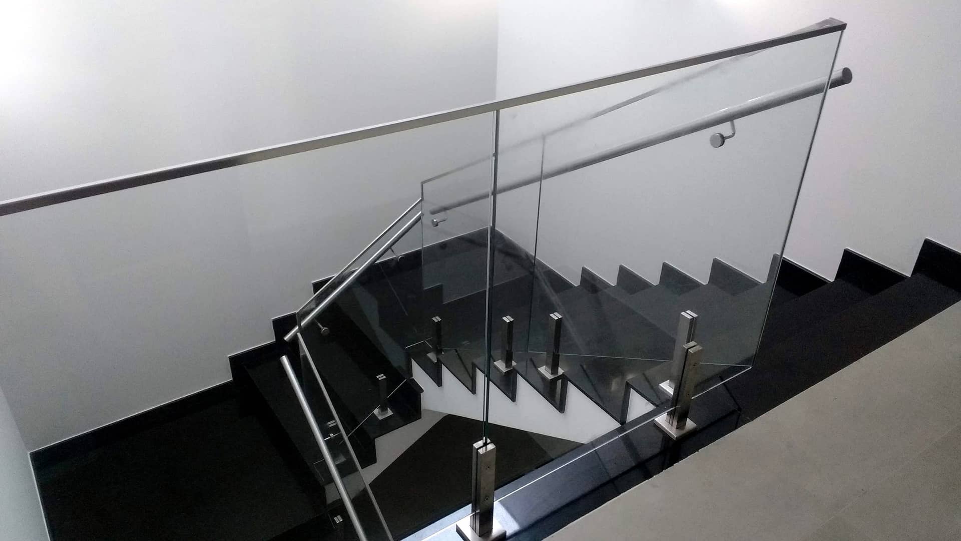 Escada em granito preto vista do alto com guarda-corpo de vidro