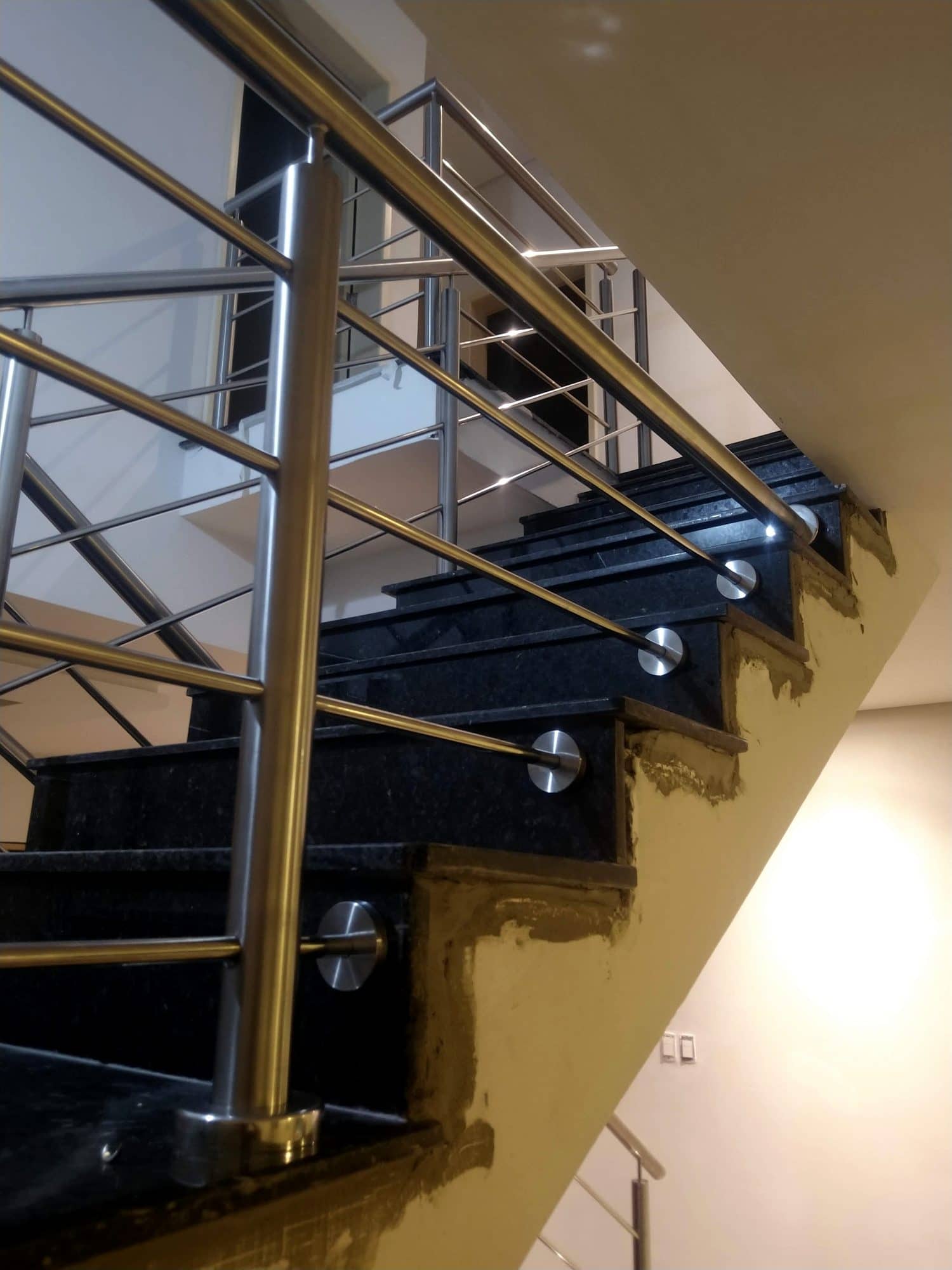 Hastes em inox acompanhando a escada de granito preto até o pavimento superior
