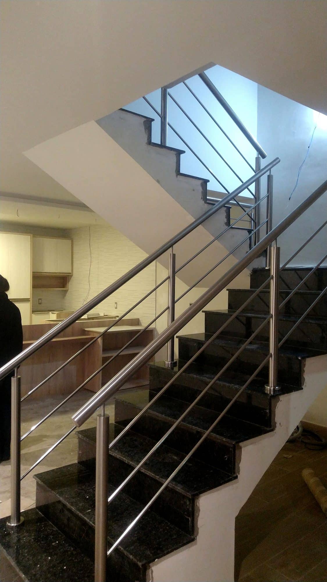 Escada de granito preto com guarda-corpo de hastes em inox junto à parede branca