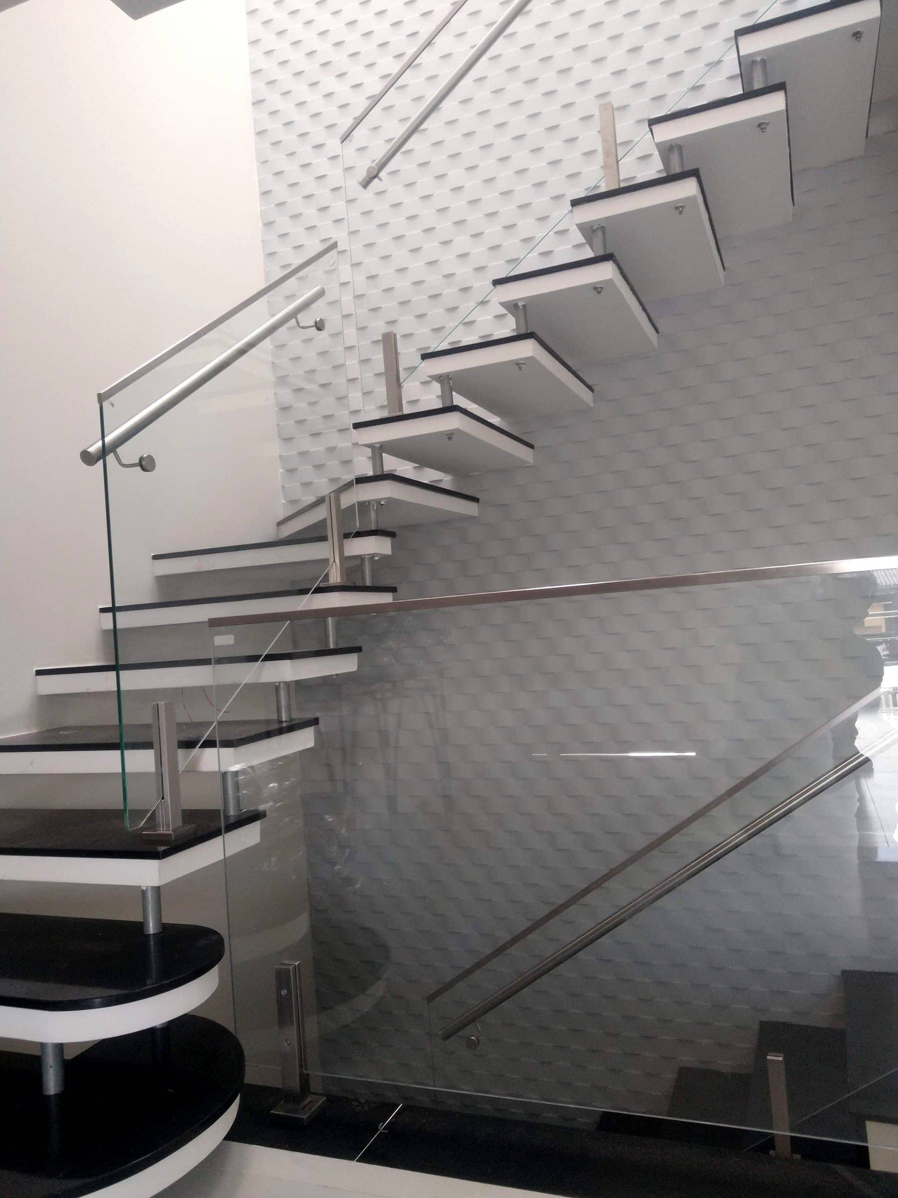 Escada com degraus escuros, guarda-corpo de vidro e corrimão tubular em inox junto a parede 3D