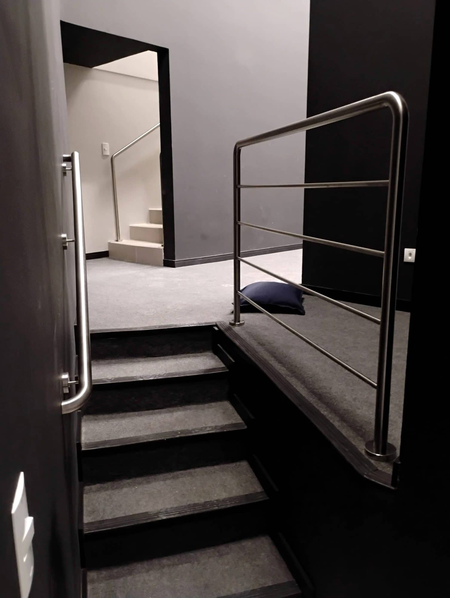 Escada com paredes escuras, corrimão de parede e guarda-corpo de hastes em inox no patamar