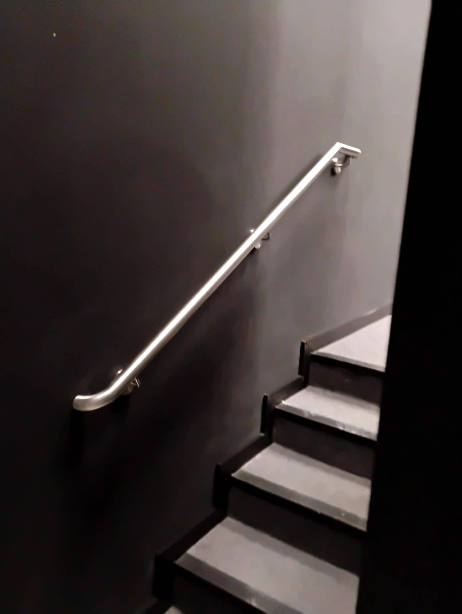 Corrimão de parede em inox acompanhando a escada entre paredes escuras