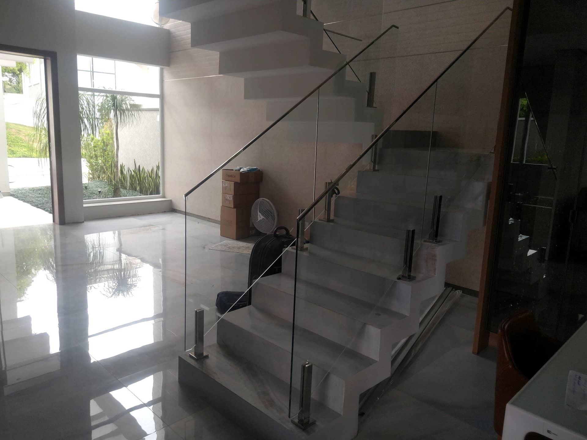 Escada branca com guarda-corpo de vidro refletida no piso de mármore