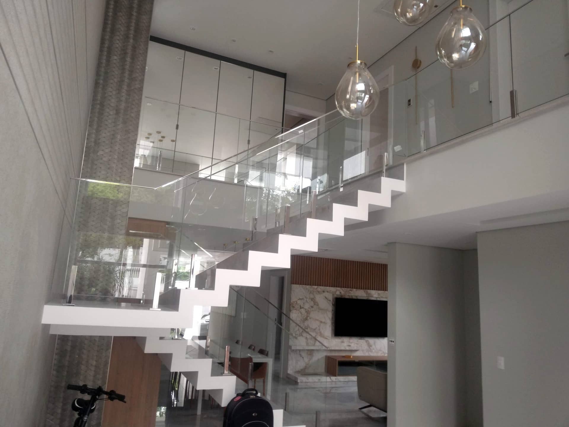 Escada e mezanino com guarda-corpo de vidro e luminárias pendentes