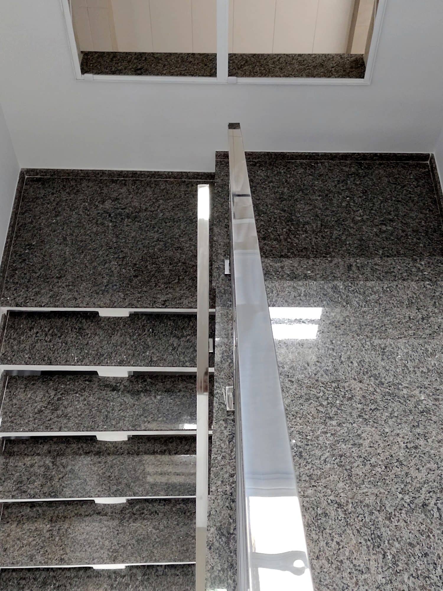 Corrimão quadrado em inox polido visto de cima, ao longo da escada de granito
