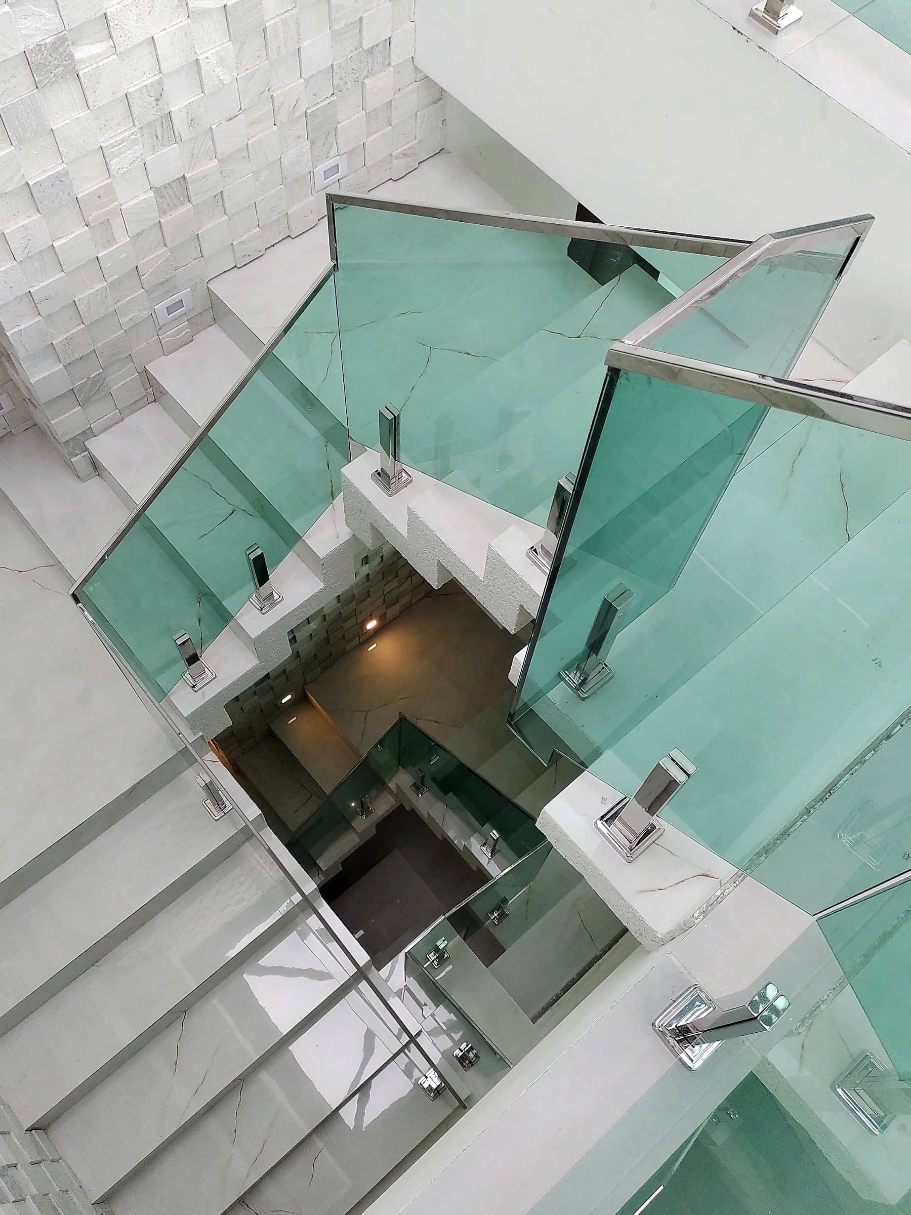 Vão da escada visto de cima, com vidro verde e colunas em inox no contorno do mezanino