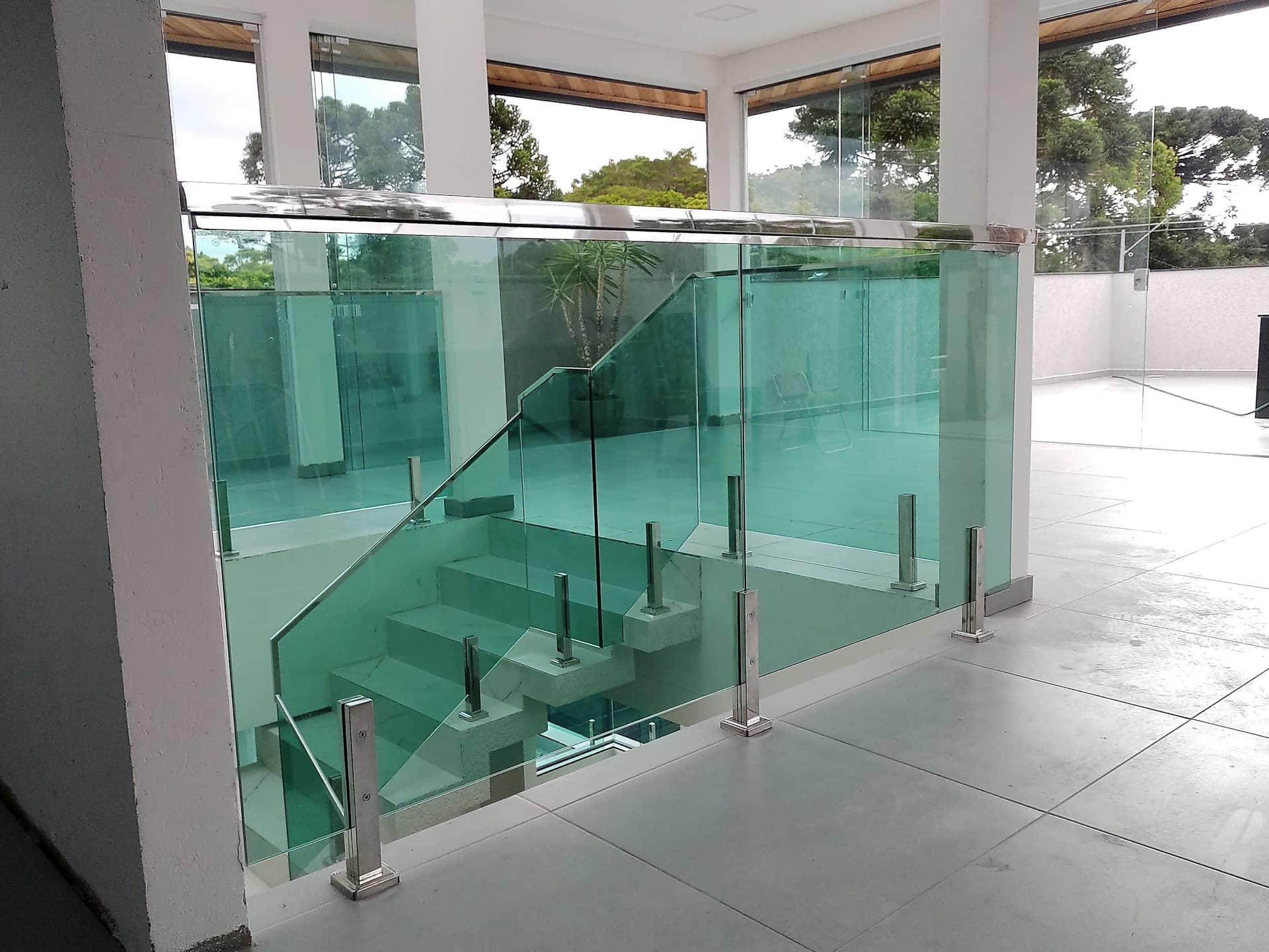 Fechamento de vão de escada em vidro verde com colunas em inox no pavimento superior