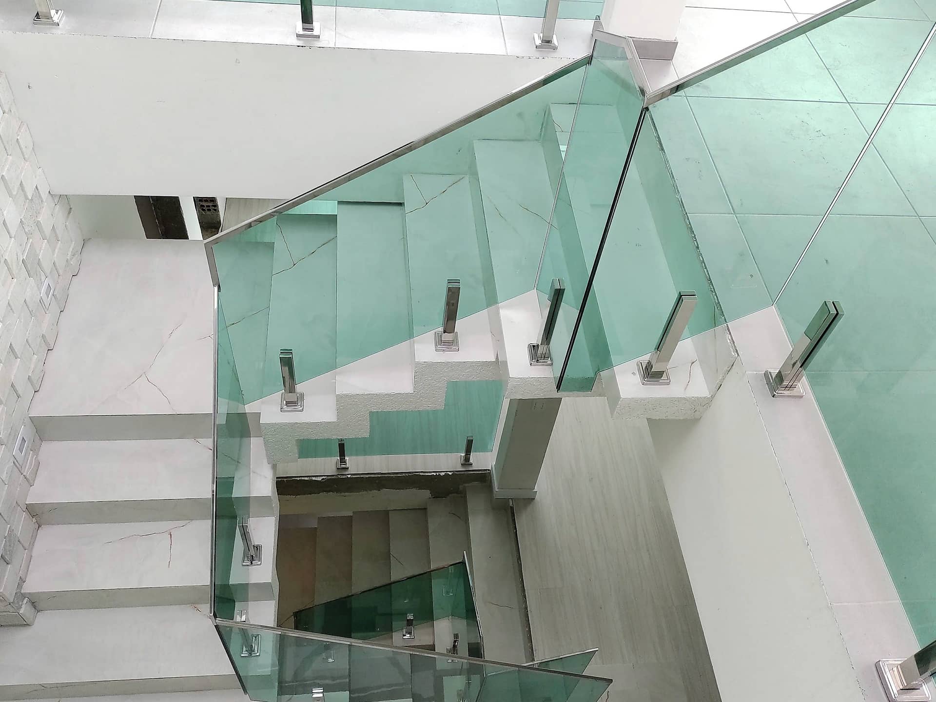 Escada vista do pavimento superior, com painéis de vidro verde e pinças em inox