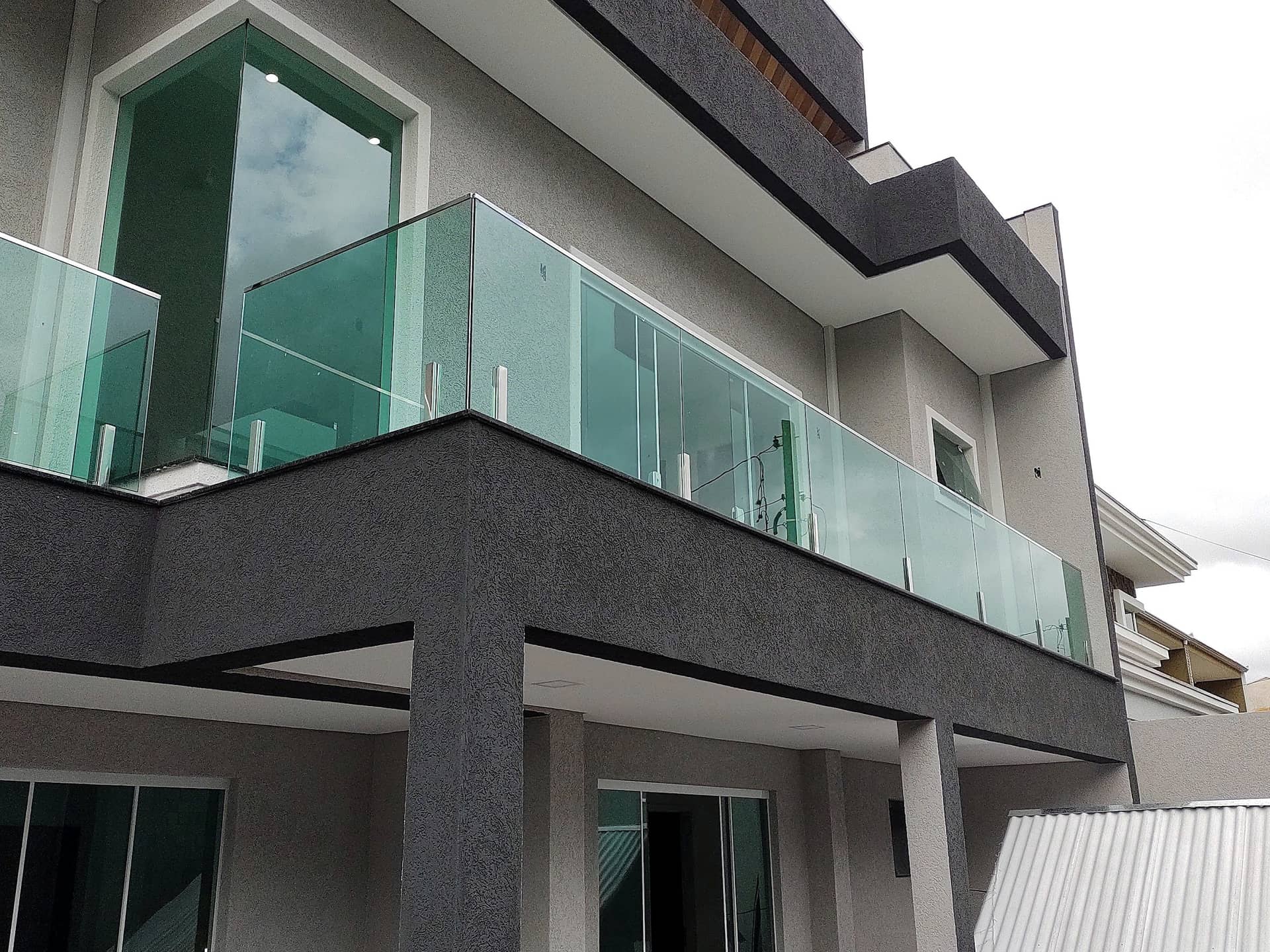 Sacada da fachada com guarda-corpo de vidro verde e colunas em inox