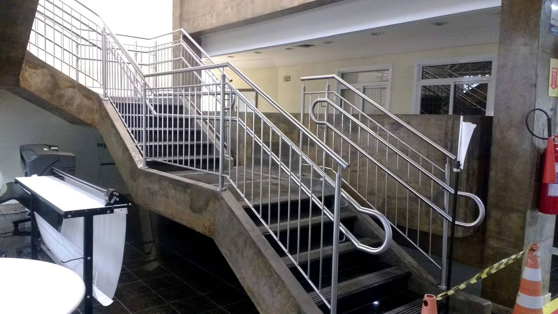 Início da escadaria com corrimão de ponta curva e guarda-corpo de travessas em inox