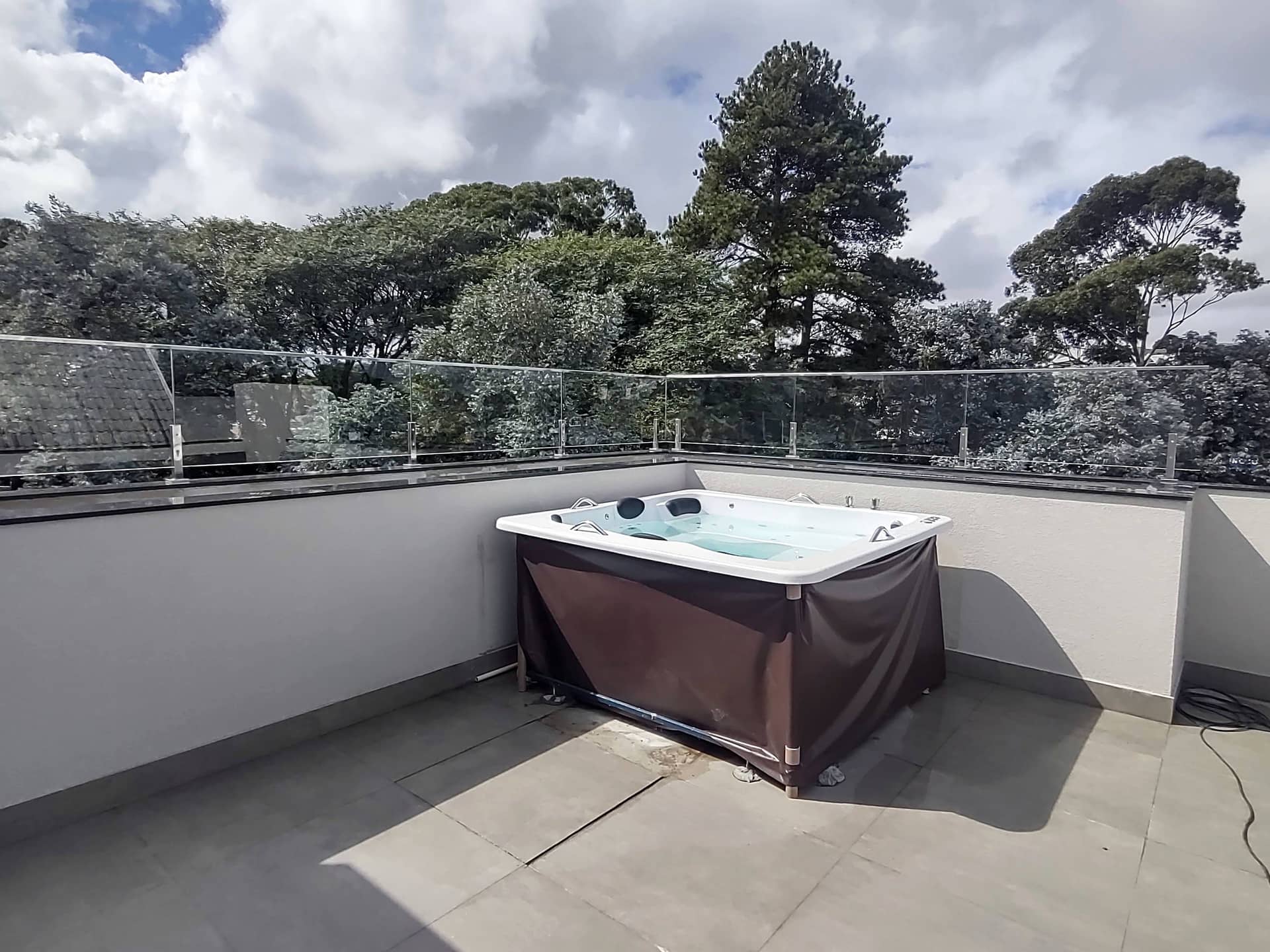 Spa na cobertura com guarda-corpo de vidro e árvores ao fundo