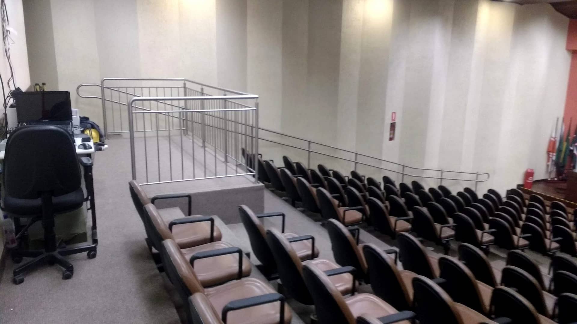 Auditório com o guarda-corpo de inox do palco visto do fundo da plateia