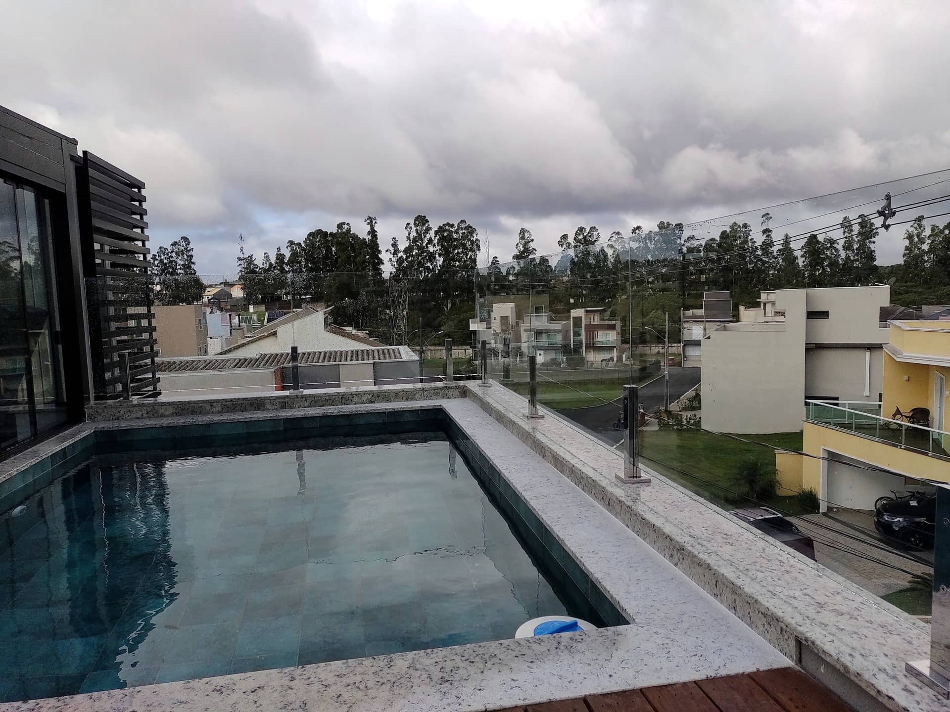 Piscina na cobertura com guarda-corpo de vidro e colunas em inox sobre a borda de pedra