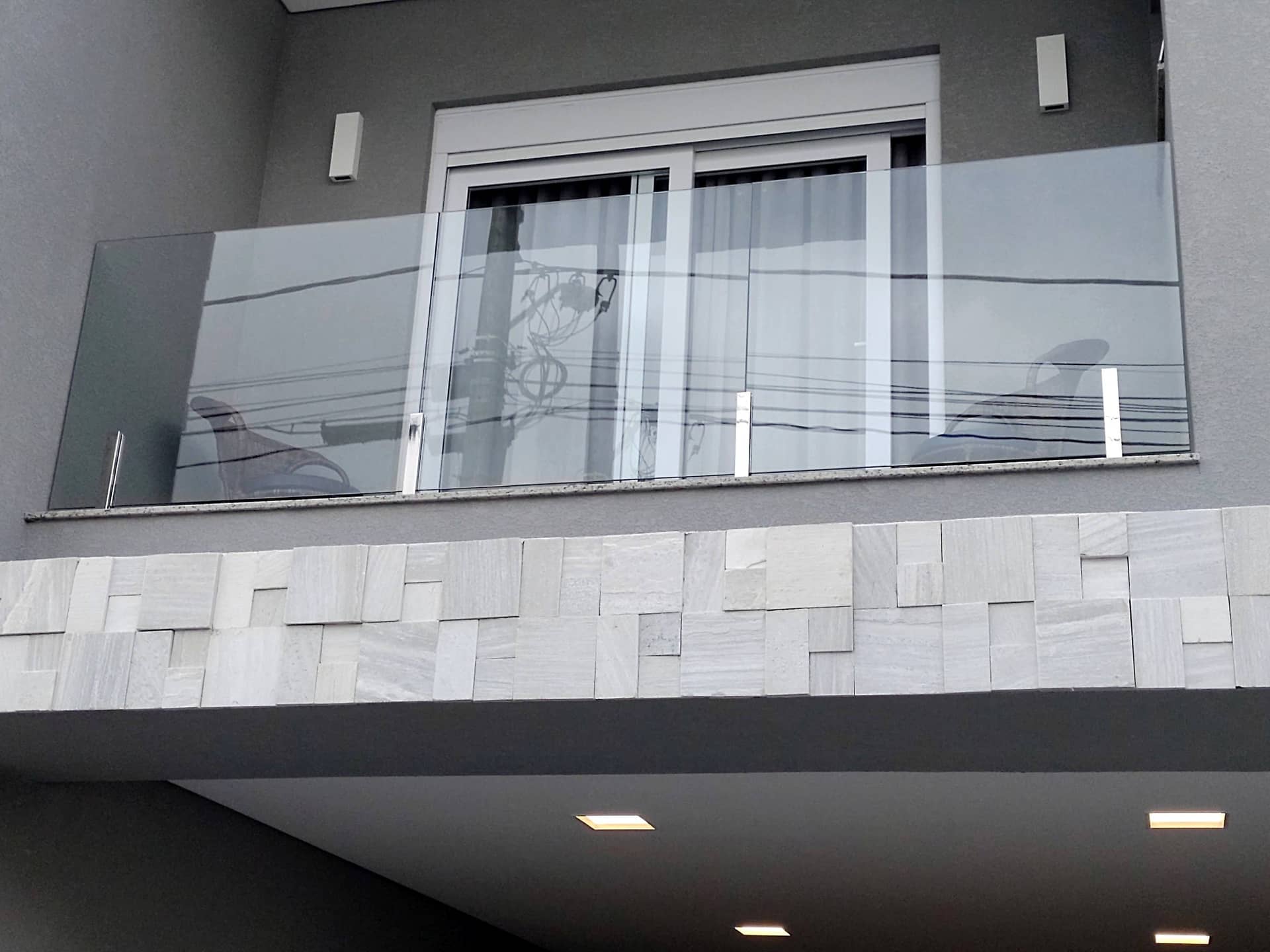 Sacada frontal com guarda-corpo de vidro e colunas em inox sobre revestimento de pedra