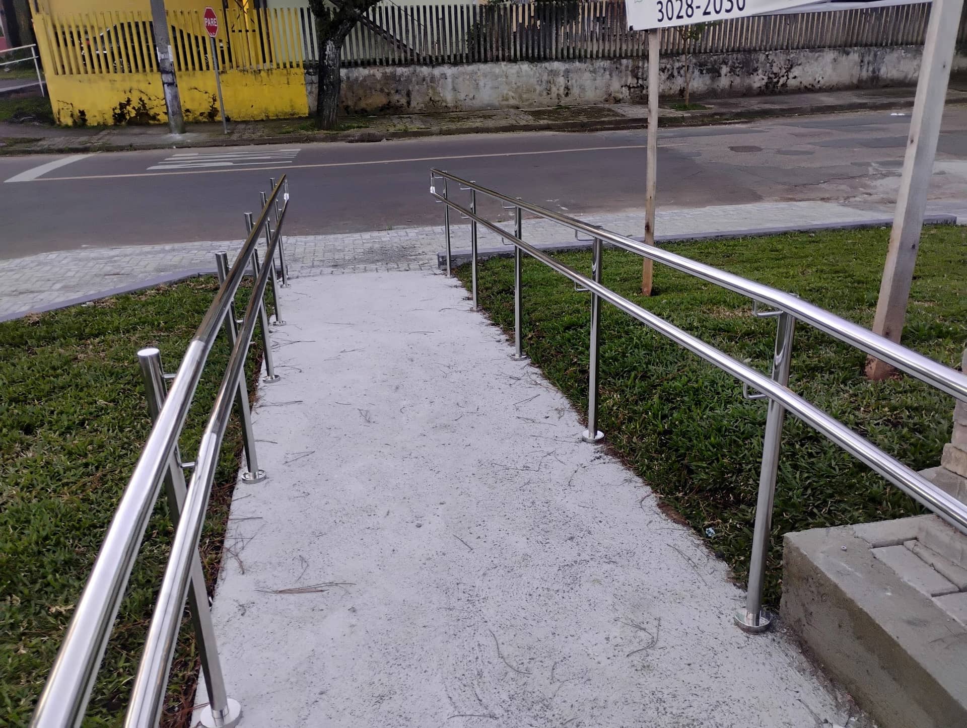 Rampa de acesso com corrimão duplo em inox dos dois lados, descendo até a calçada
