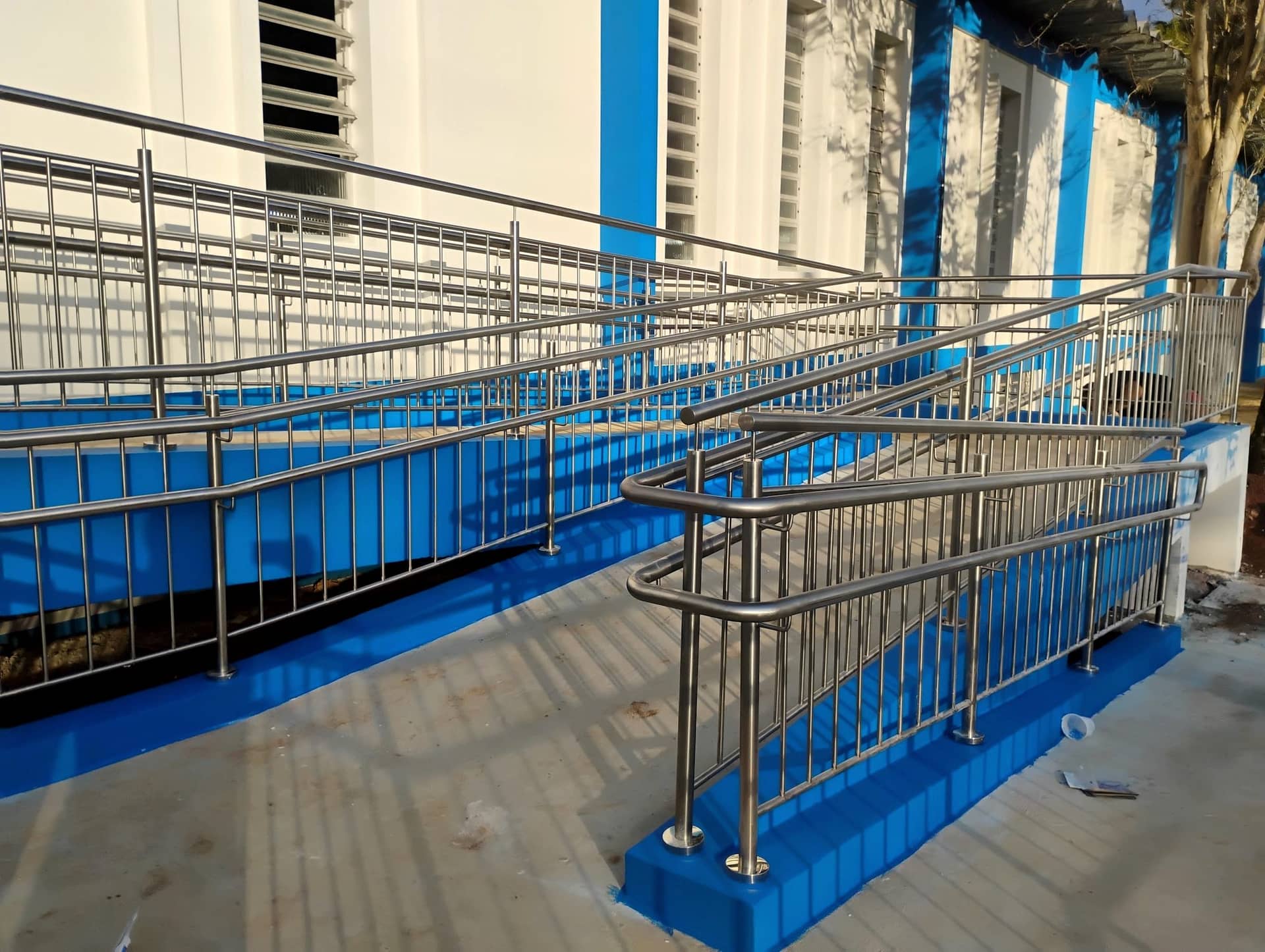 Rampa externa com guarda-corpo de travessas verticais e corrimão duplo em inox