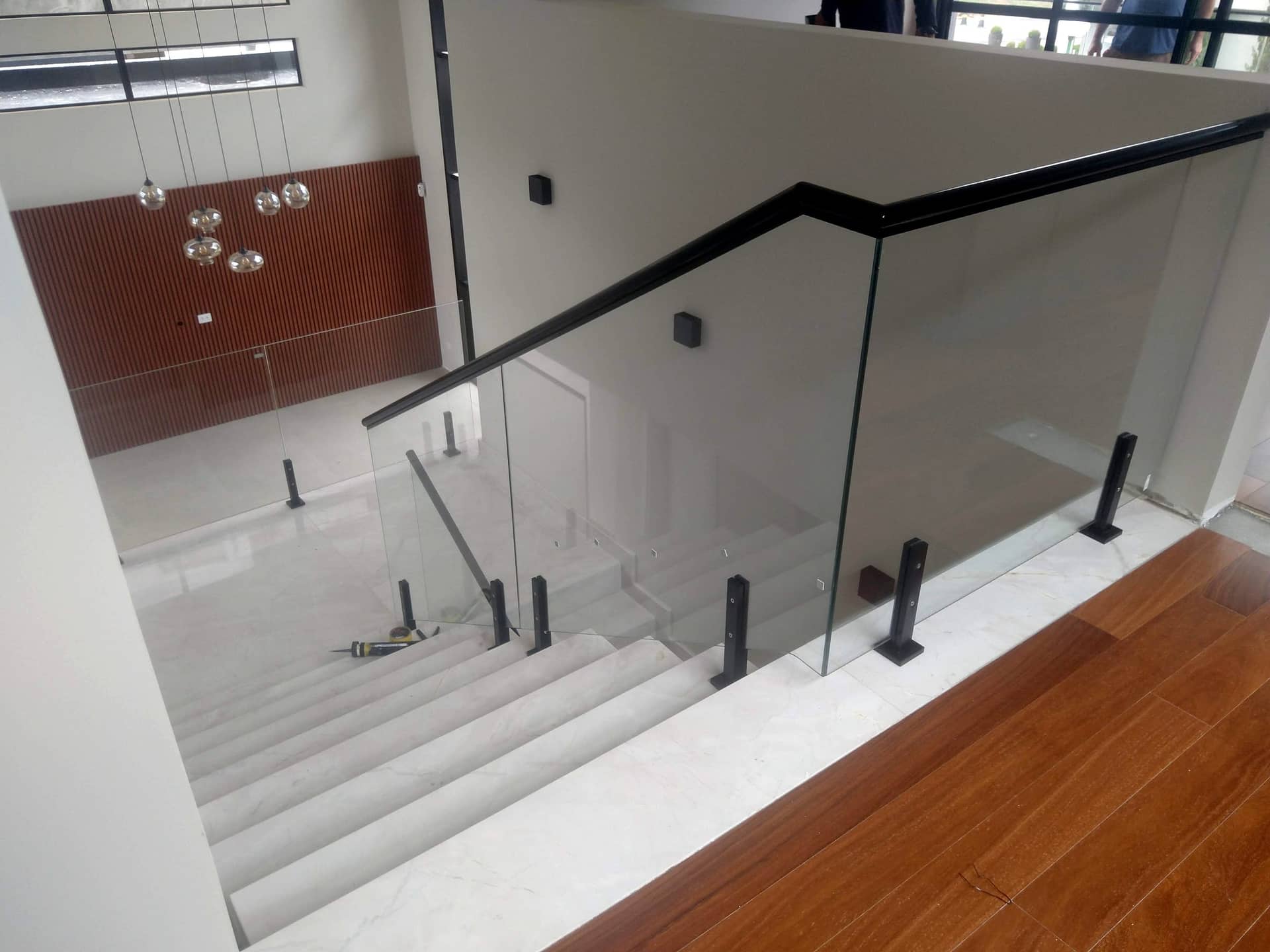 Escada interna com vidro, colunas e corrimão pretos sobre piso de madeira