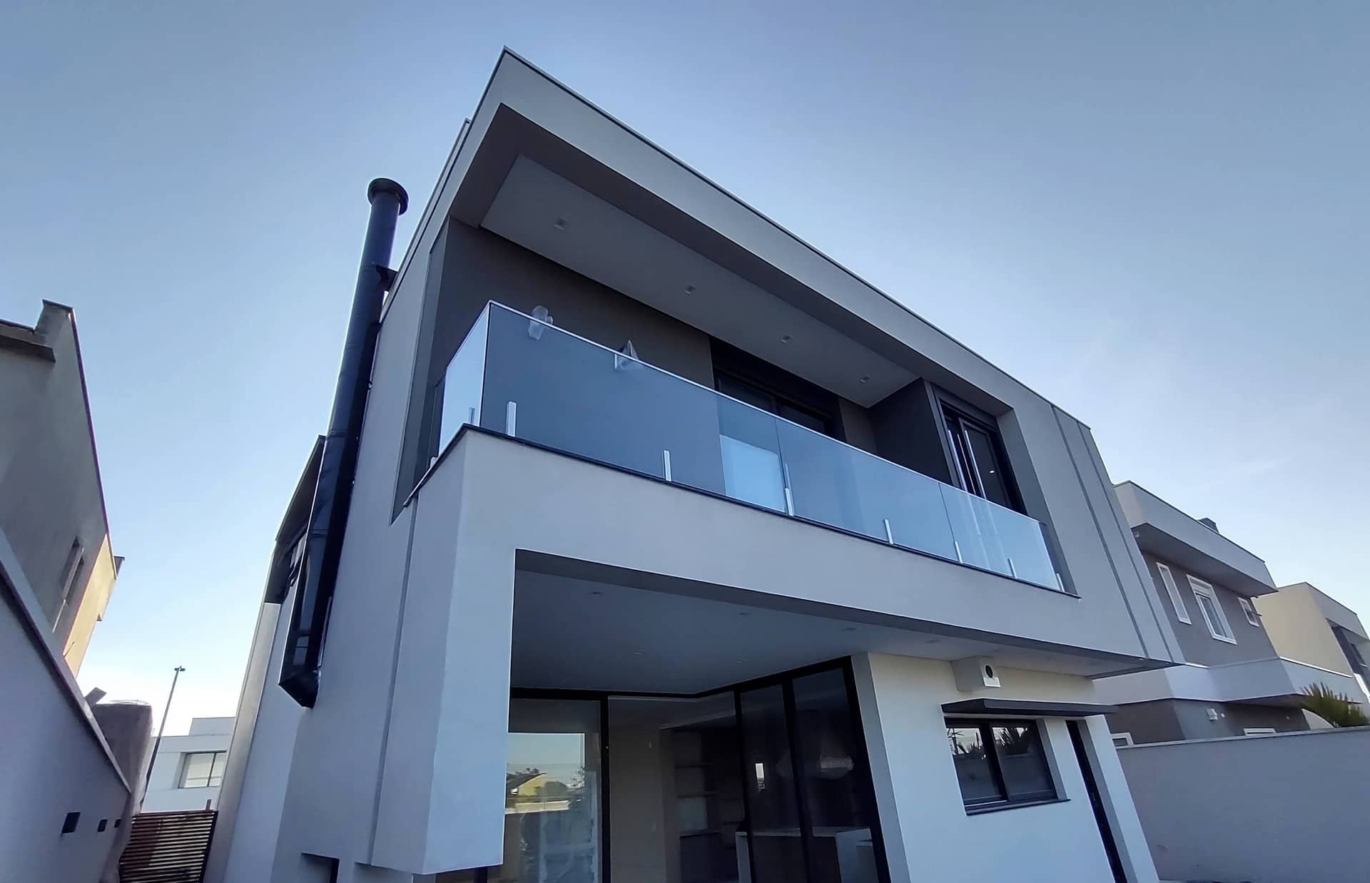 Fachada com sacada em vidro e colunas em inox sob céu azul