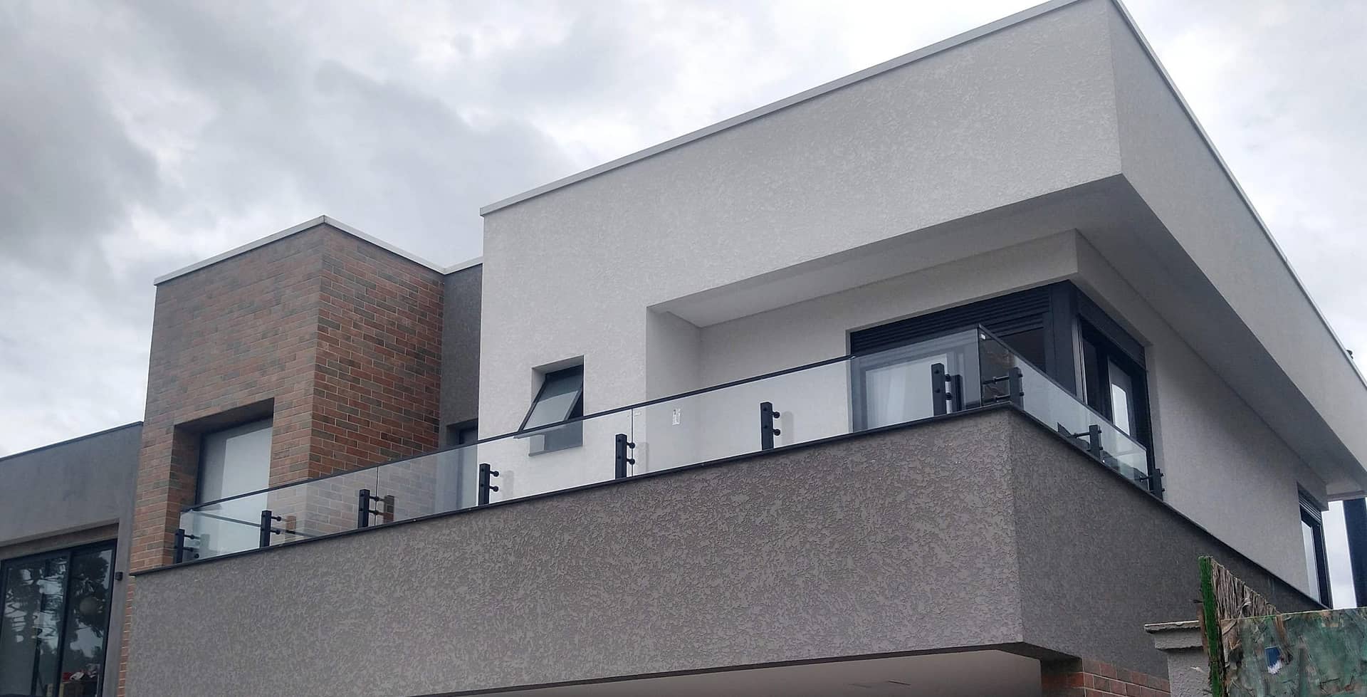Sacada com vidro fixado na lateral da laje em fachada de tijolo e textura
