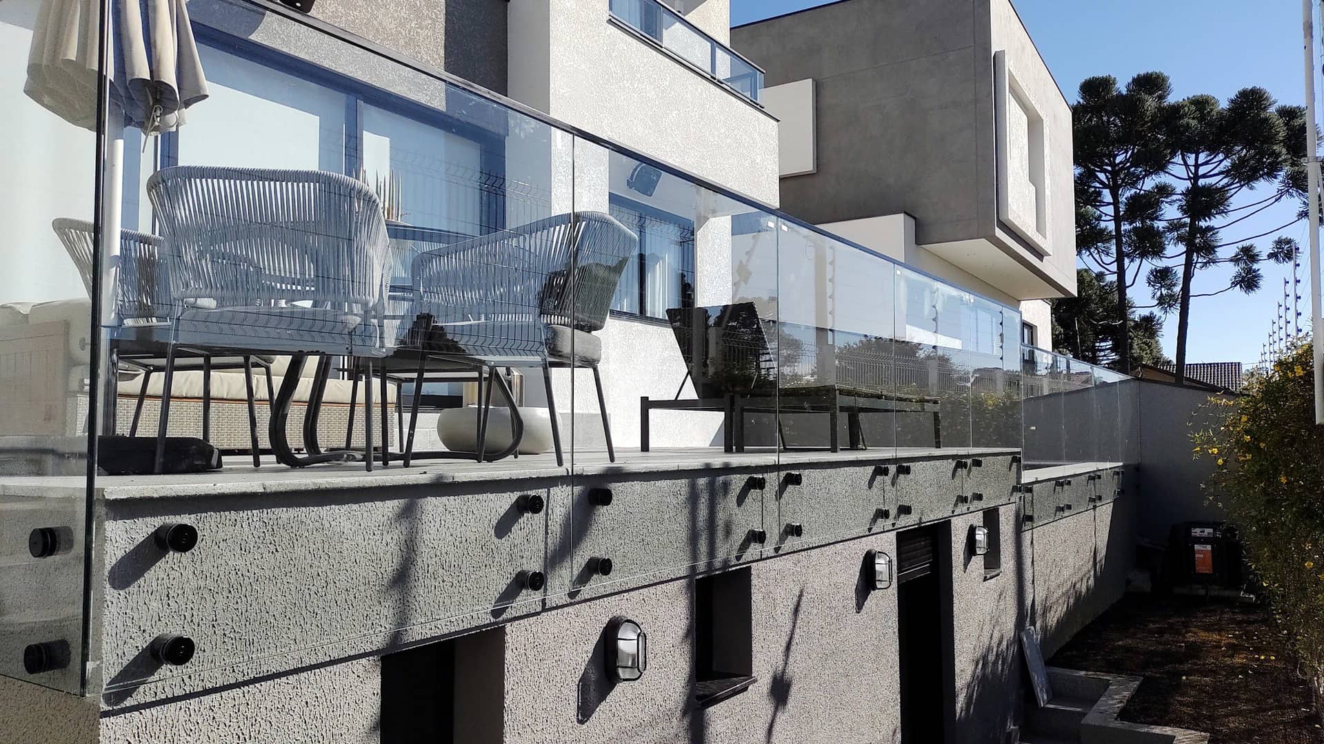 Guarda-corpo de vidro do terraço visto de baixo, com as pinças em inox aparentes na face da laje