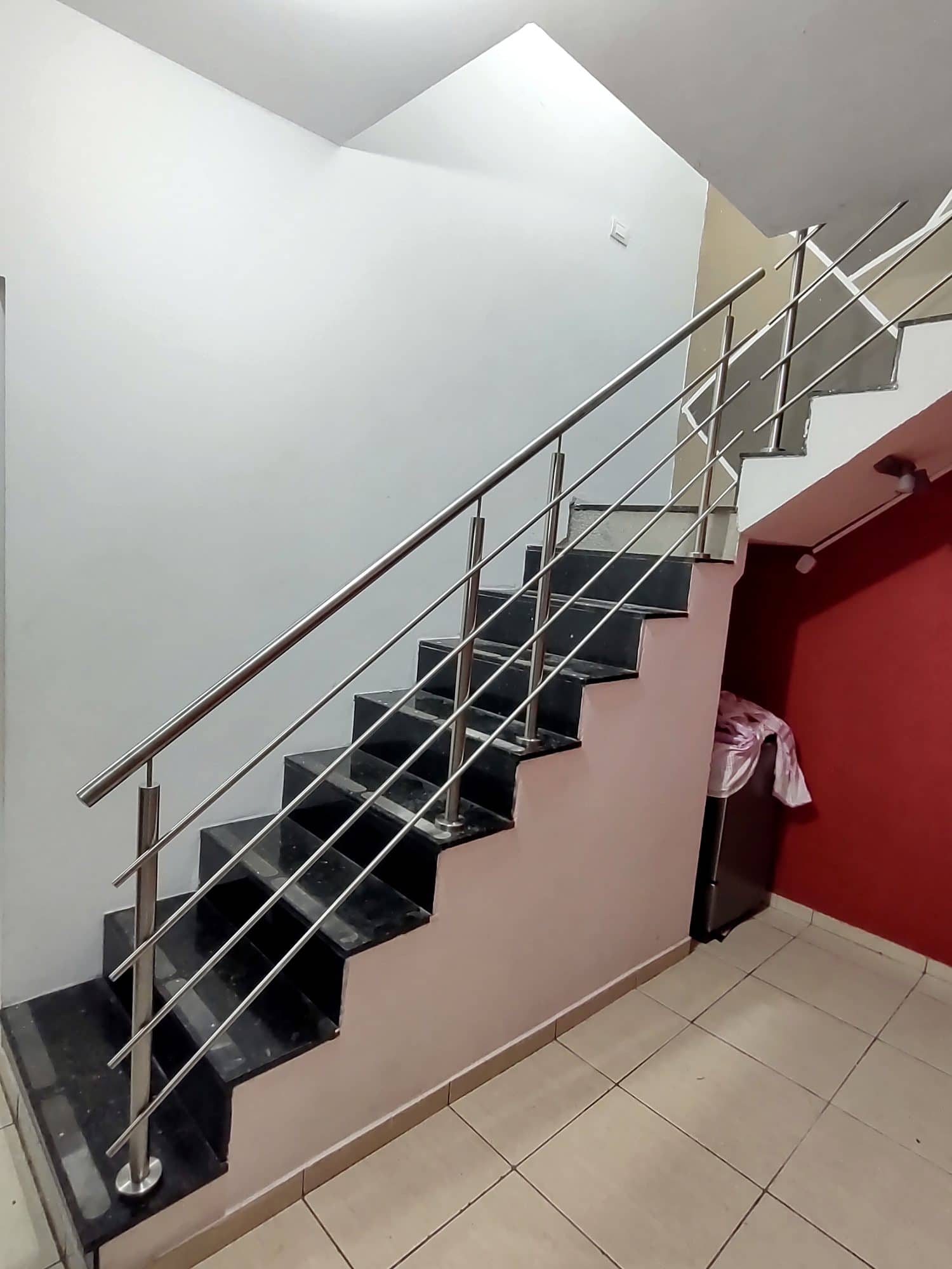 Escada em granito preto com guarda-corpo de hastes horizontais em inox junto à parede vermelha