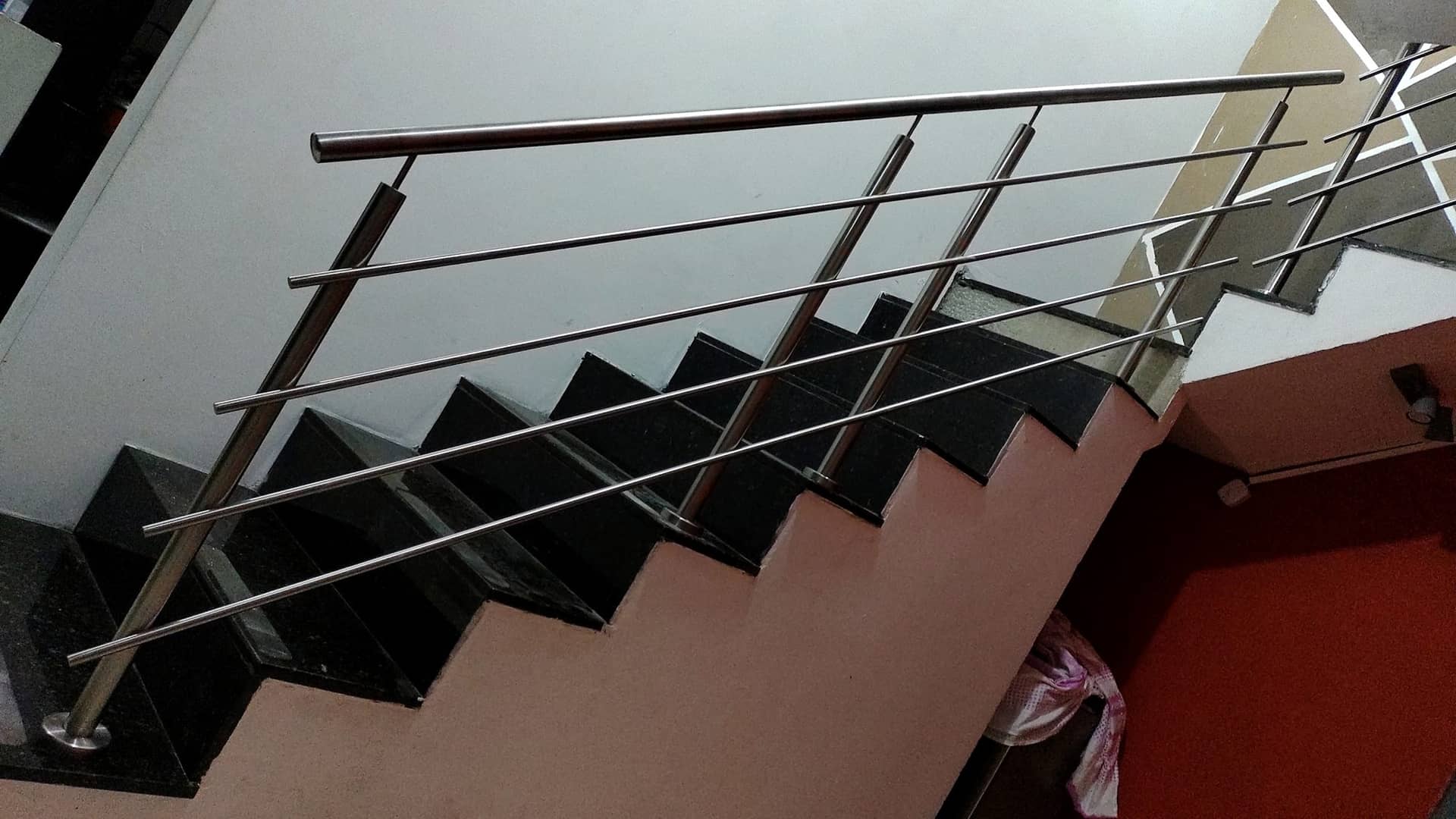 Hastes horizontais em inox acompanhando a escada em granito preto