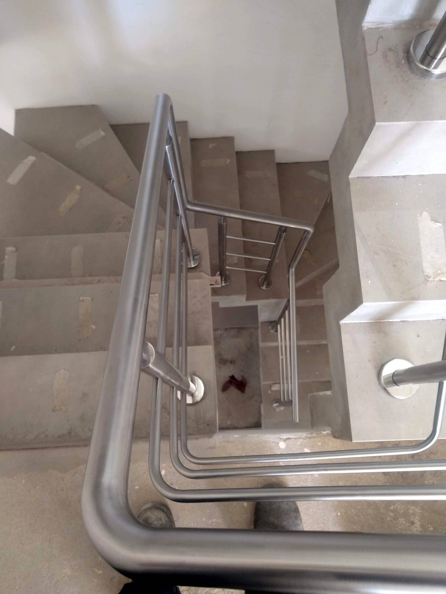 Corrimão em inox contornando o vão de uma escada, visto de cima