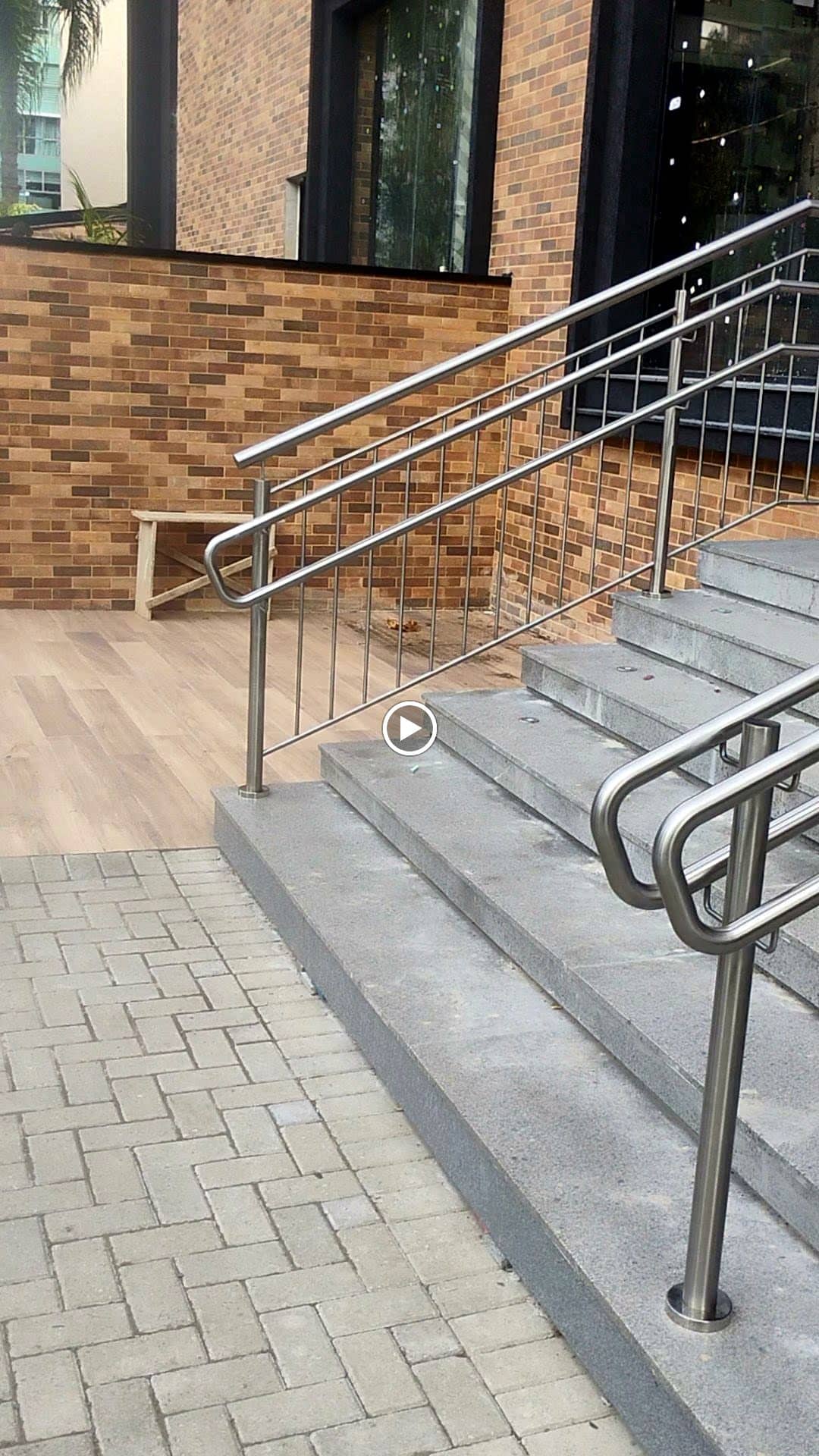 Escada externa com corrimão e travessas verticais em inox junto à parede de tijolo