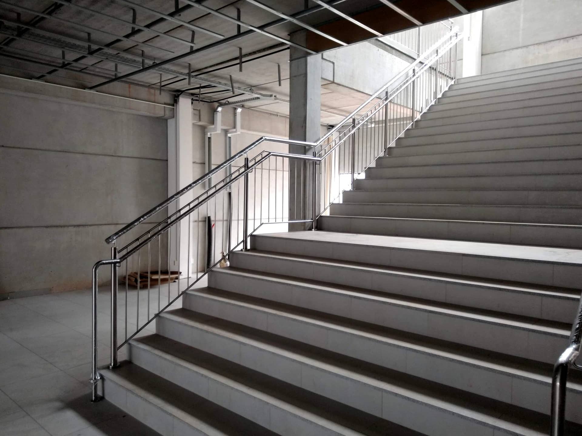 Escadaria interna larga com corrimão central em inox