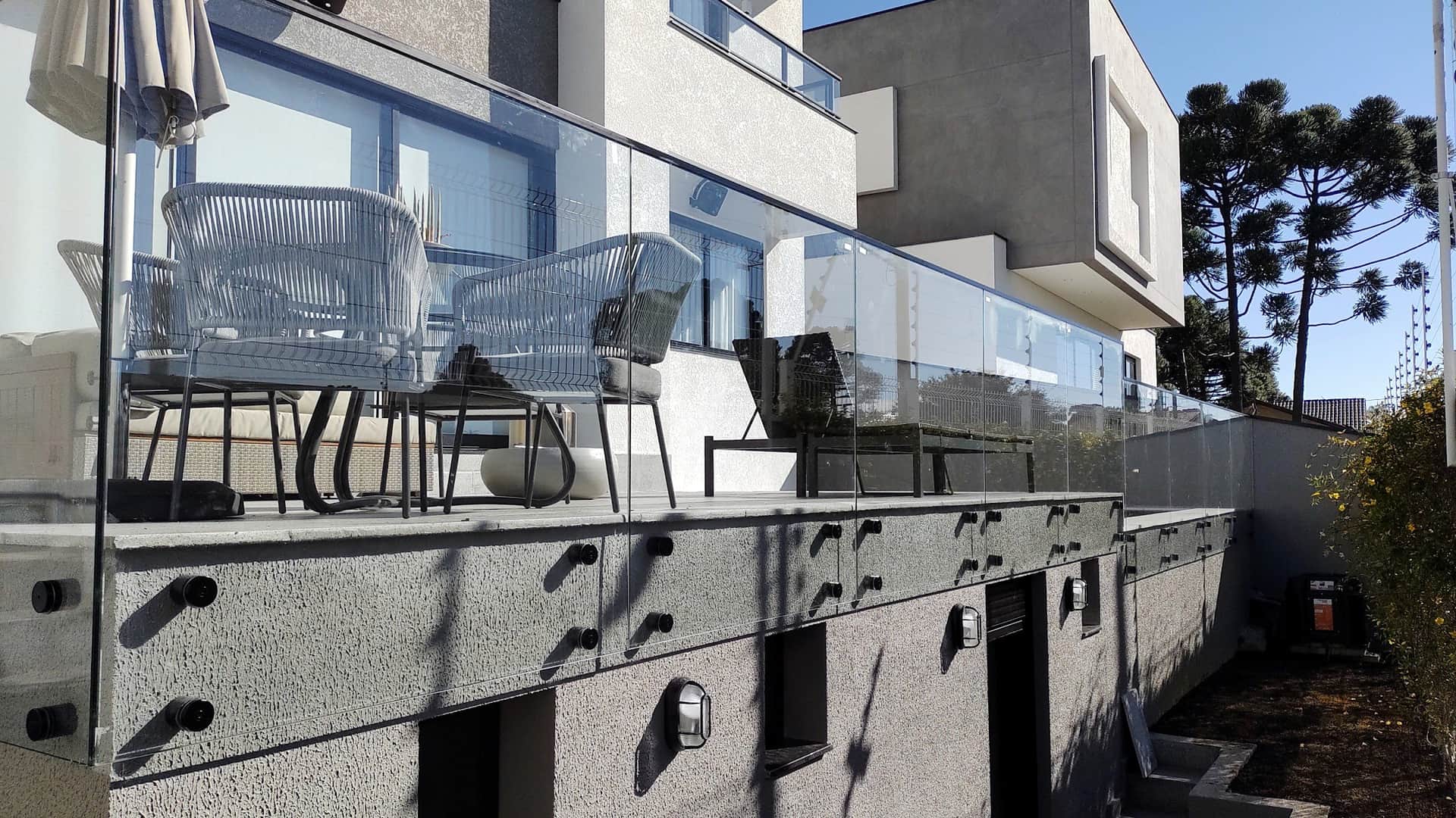 Guarda-corpo de vidro do terraço visto de baixo, com as pinças em inox aparentes na face da laje